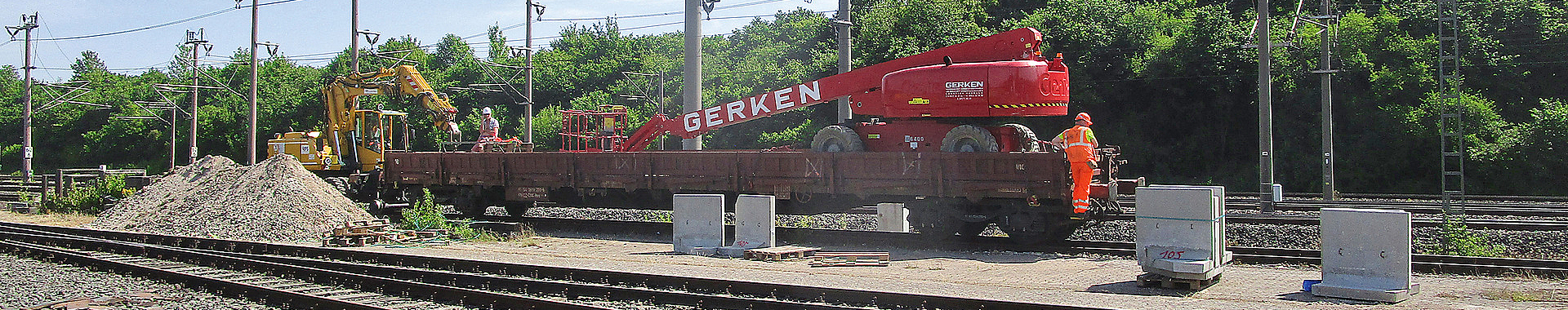 Zwei Bauarbeiter auf einem Güterwagen in einer Gleisbaustelle.