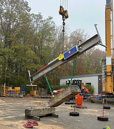 Die Ludwig Traverse von Ludwig System ist eine der Lastausgleichsvorrichtungen, die in Feuchtwangen getestet wurde. Schräg hängende, längliche Lastausgleichseinrichtung, an der ein mit zwei Seilen befestigtes Betonteil häng.