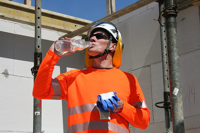 Ein Bauarbeiter mit UV-Schutzkleidung trinkt eine Flasche Wasser.