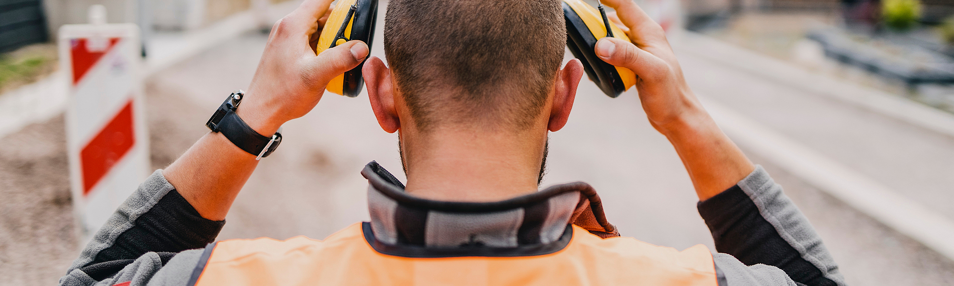 Blick auf einen Bauarbeiter von hinten, der seinen Gehörschutz aufsetzt.