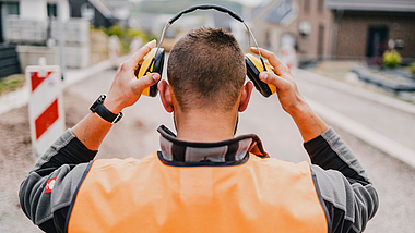 Blick auf einen Bauarbeiter von hinten, der seinen Gehörschutz aufsetzt.