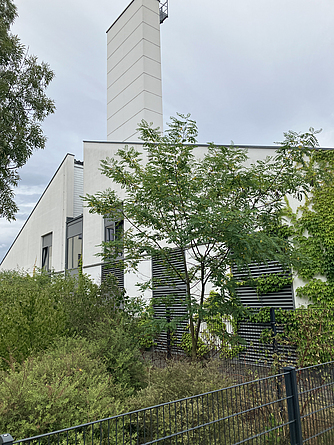 Gebäude mit Schornstein in einem begrünten Areal, das umzäunt ist.