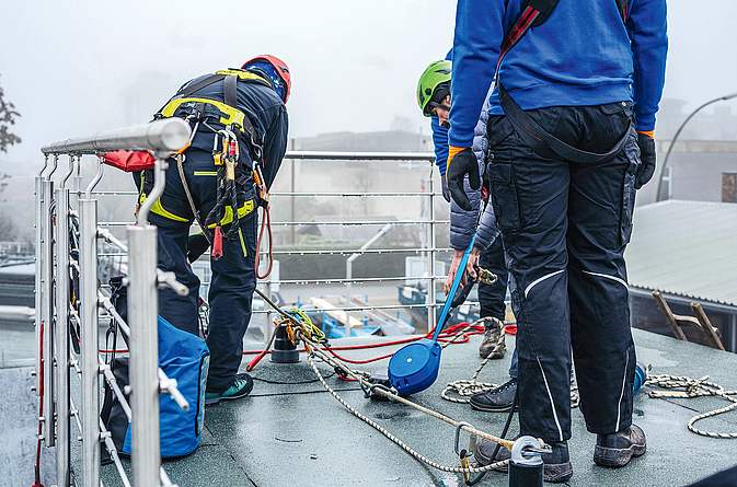 Dachdecker bei der Unterweisung mit Persönlicher Schutzausrüstung gegen Absturz auf einem Flachdach.