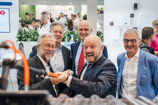 Ein Mann probiert eine Teleskopstange an einem provisorischen Dach in einer Messehalle aus, vier Männer stehen um ihn herum.