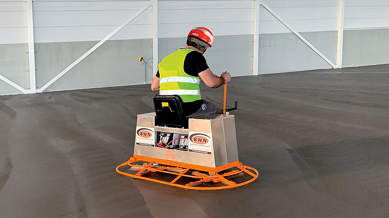 Ein Mann mit Schutzhelm und Warnweste steuert einen Doppelglätter.