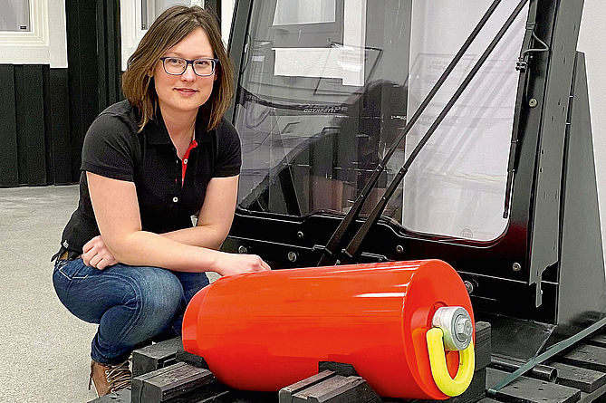 Malin Påhlson, die bei Hammerglass als Senior Design & Compliance Engineer arbeitet, vor einer Kabine mit FOPS- getesteten RABS-Rahmen Eine Frau kniet vor einer Fahrerkabine.