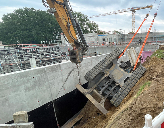 Ein an einer geböschten Baugrube umgestürzter Bagger wird mit einem Kran herausgezogen.