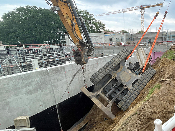 Ein an einer geböschten Baugrube umgestürzter Bagger wird mit einem Kran herausgezogen.