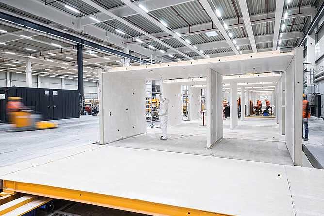 Vorfertigung eines Moduls im Werk von Max Bögl. Eine Person im weißen Schutzanzug bearbeitet gerade die Decke des Moduls.