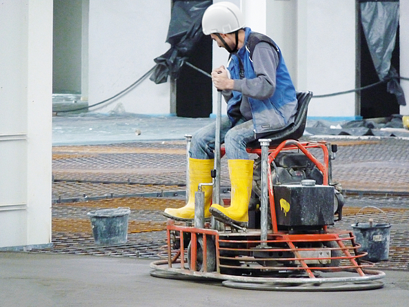 Glätten von Estrich oder Betonflächen Ein Mann mit Schutzhelm steuert einen bezinbetriebenen Glätter.