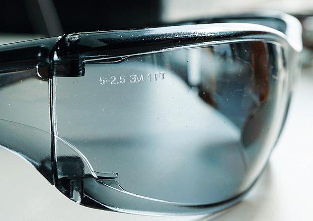 Beispiel einer Sonnenbrille mit Kennzeichnung „5-2,5 1 FT“ (Baustellen-tauglich) Nahaufnahme einer Sonnenbrillen-Fassung: Das Brillenglas aus farblos-transparentem Kunststoff trägt die eingeprägte Kennzeichnung „5-2,5 3M 1 FT“ und ist somit baustellen-tauglich.