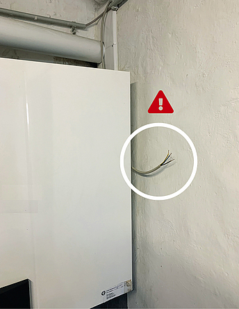 Eine Gastherme ist an einer Wand befestigt. Direkt neben ihr liegt eine unisolierte Elektroleitung frei.