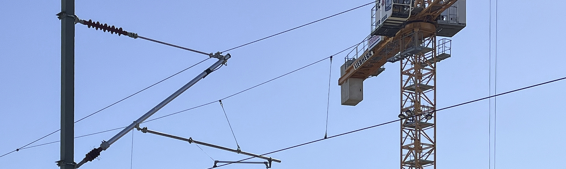 Oberleitungen, hinter denen das obere Teil eines Krans zu sehen ist.