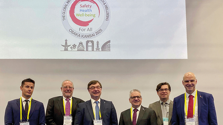 Internationales Symposium der
ISSA Construction in Osaka Sechs Männer in Anzügen stehen vor einer Leinwand mit dem Logo und Motto des Weltkongresses für Sicherheit und Gesundheit bei der Arbeit 2025 in Osaka.