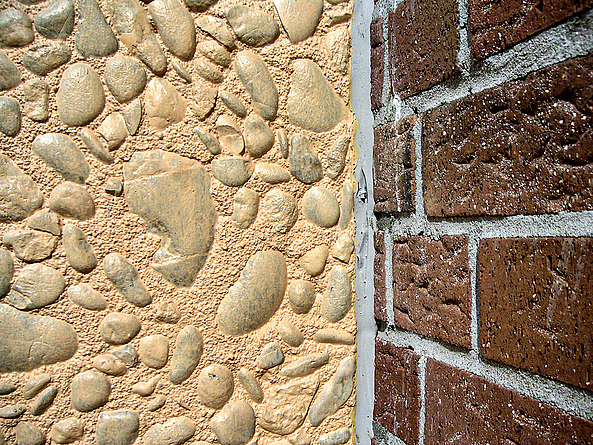 Zwei Mauerwerke nebeneinander. Dazwischen sind Fugen zu erkennen. Die eine Mauer ist mit Steinen, die andere mit Ziegeln verblendet.