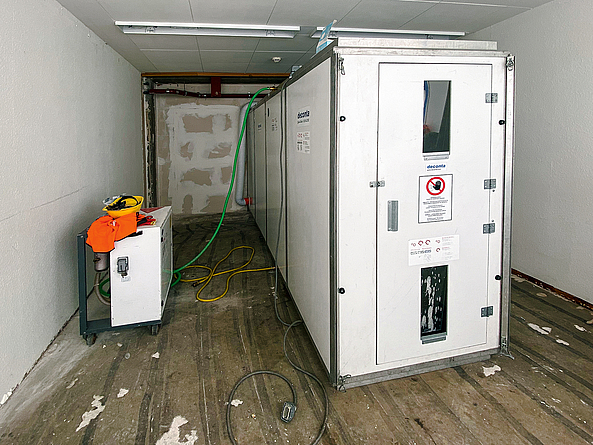 Personenschleuse für den Übergang vom kontaminierten (Schwarz-)Bereich in nicht belastete Bereiche Kastenförmige Personenschleuse ragt in einen schmalen Raum.