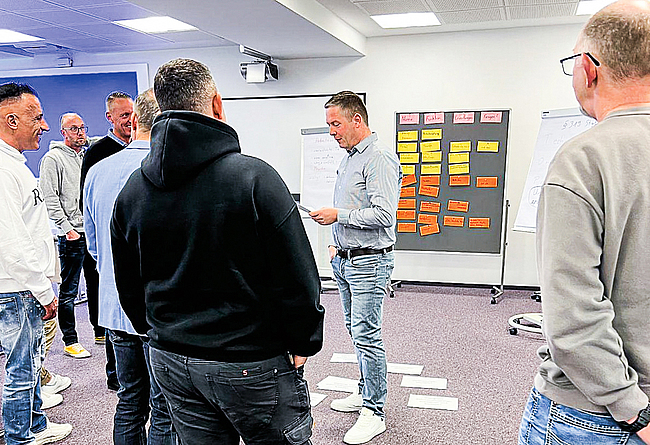 Die gemeinsame Erarbeitung von Inhalten ist wesentlicher Bestandteil des Seminars. Eine Gruppe steht im Halbkreis um einen Mann herum, der etwas erklärt.