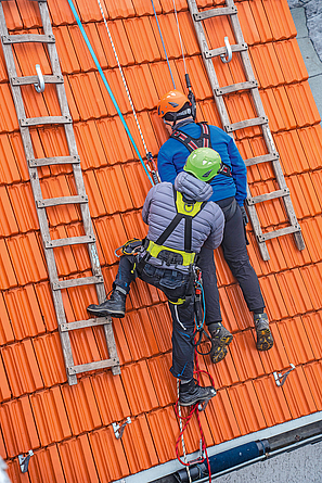 Trainer mit Dachdeckern bei der Unterweisung für Persönliche Schutzausrüstung gegen Absturz. 