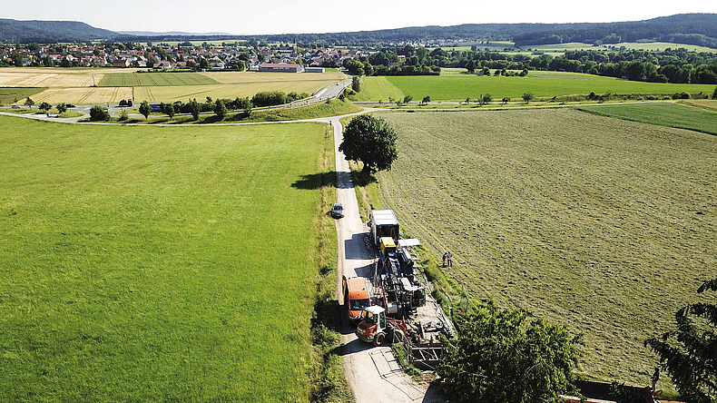 Auf einem Weg zwischen grünen Feldern stehen mehrere große Baumaschinen.