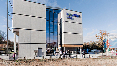 Modernes, mehrstöckiges Gebäude mit großer Glasfront. An der Seite ist der Schriftzug "Building Lab" angebracht.