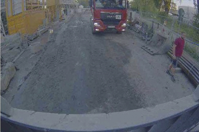 Screenshot des Kamerabildes, welches ein Bauzeug hinter dem Radlader auf einem engen Fahrweg auf einer Baustelle zeigt.