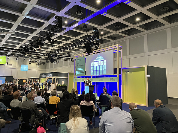 Mann auf einem Podium hält vor Publikum einen Vortrag.