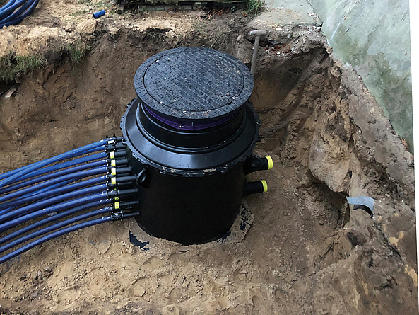 Kabelschacht mit mehreren blauen Leitungen in einer Baugrube.