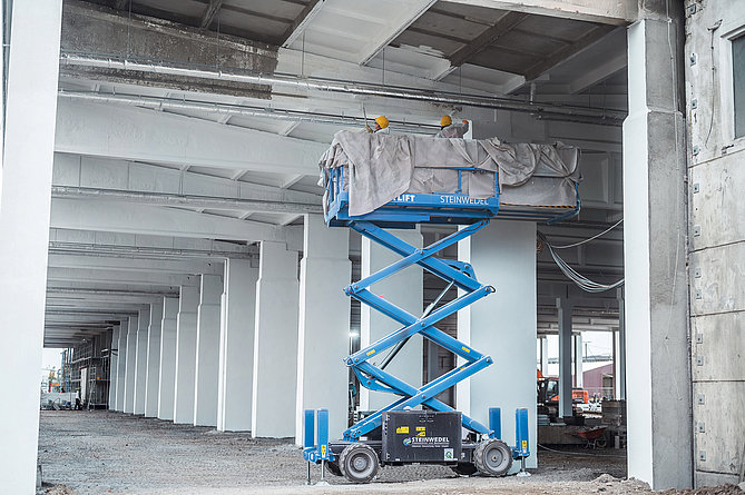 Zwei Personen auf einem Hubsteiger streichen Deckenunterseite und Binder.