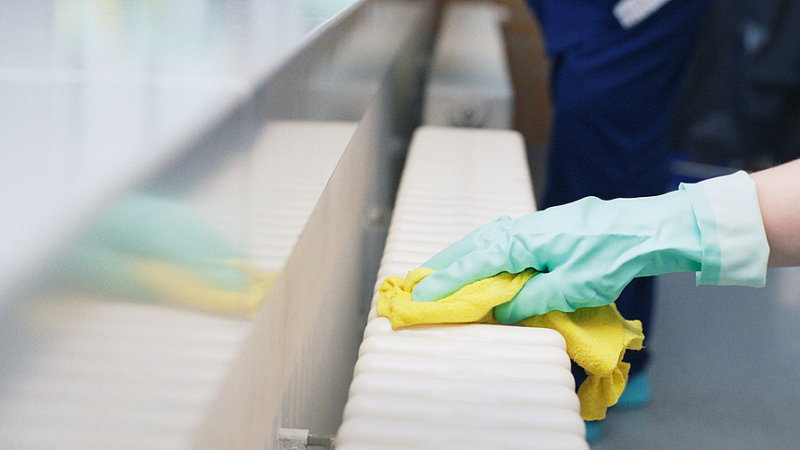Zwei Reinigungsfachkräfte wischen mit Handschuhen und Lappen glatte Oberflächen ab.
