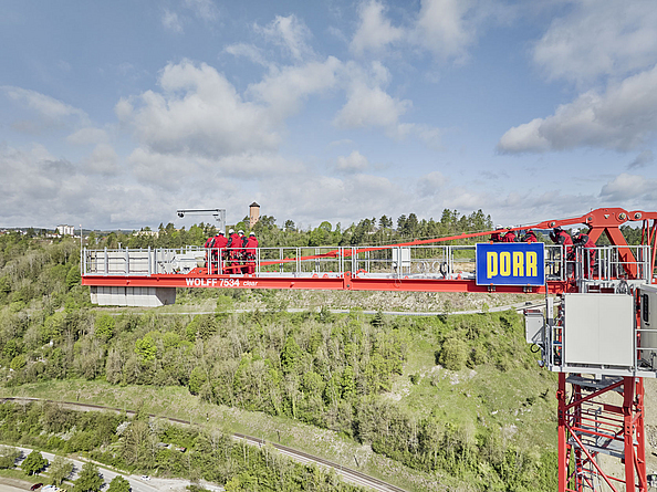 Training Höhenrettung auf Kran an Baustelle Hochbrücke Horb  Eine Gruppe von Personen in roter Schutzkleidung und Helm befindet sich auf dem Ausleger eines hohen Krans.