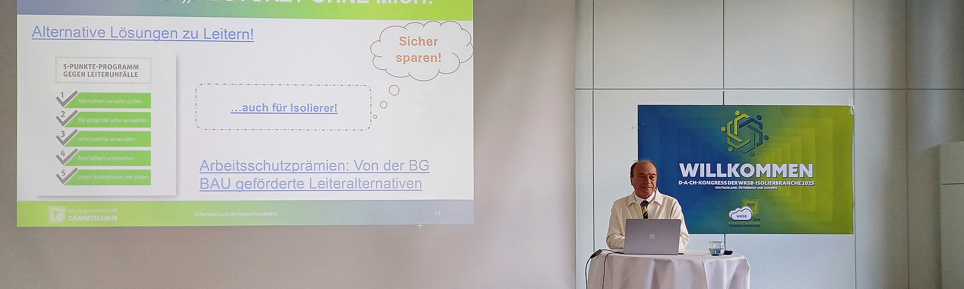 Bernd Merz beim D-A-CH-Kongress der WKSB-Isolierbranche 2025 Bernd Merz steht an einem Rednertisch auf einem Podium. Vor ihm ist ein Laptop geöffnet, auf der Leinwand hinter ihm ist eine Folie zum Thema Absturz zu sehen.