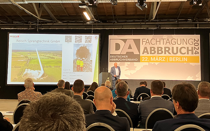 Eduard Reisch stellte Beispiele für Sprengfaltung vor. Ein Mann referiert auf dem Podium, hinter ihm sind zwei Leinwände zu sehen.