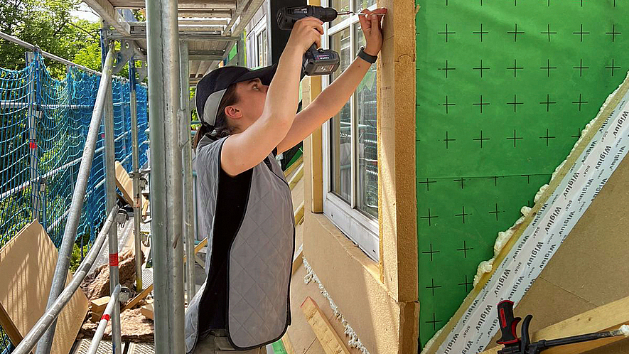 Bauarbeiterin auf einer Baustelle an einem sonnigen Tag. Sie trägt eine Kühlweste und ein Kühl-Cap.