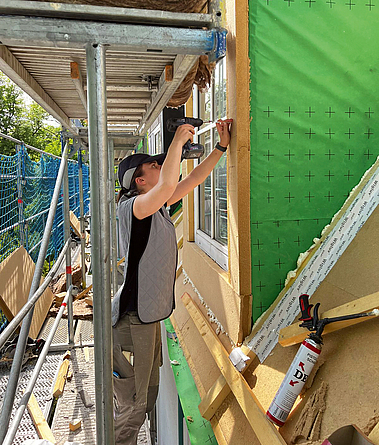 Bauarbeiterin auf einer Baustelle an einem sonnigen Tag. Sie trägt eine Kühlweste und ein Kühl-Cap.