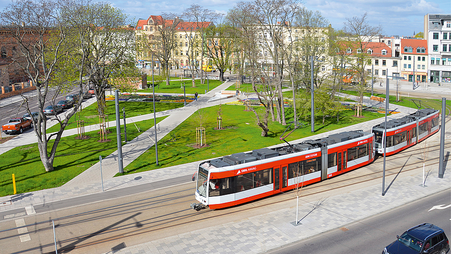 Eine Straßenbahn hält vor einem begrünten Platz in einem Wohngebiet.