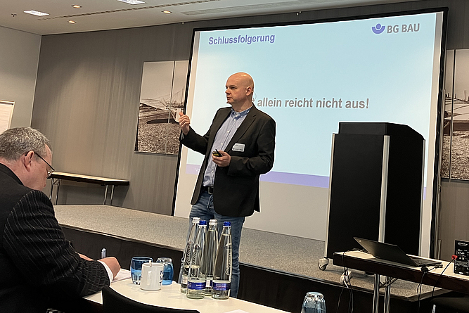 Volker Münch, Leiter Referat Tiefbau, BG BAU Prävention Ein Mann vor einer Präsentationswand hält einen Vortrag.