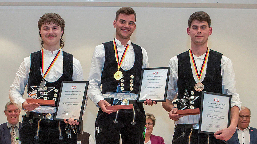 Drei Dachdecker stehen auf einem Siegerpodest und halten Urkunden und Medaillen.