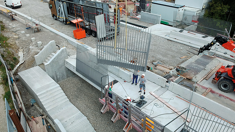 Ein hohes Stahl-Geländer wird am Kran auf eine Baustelle hinab gelassen.