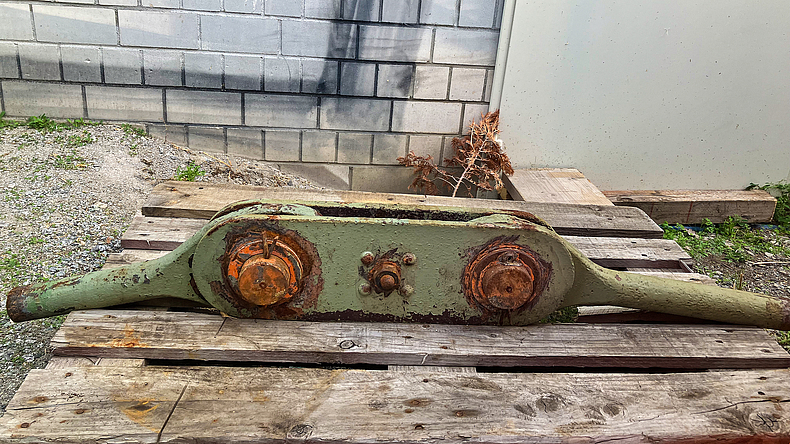 Altes Zugband aus dem Ostbahnhof bzw. der gelenkige Verbinder, der dafür sorgt, dass keine Spannung in das System kommt. Altes, teilweise verrostetes Verbinderelement mit zwei Schrauben auf einer Holzpalette.
