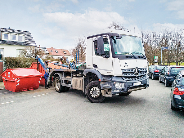Der Kran-LKW eines Recycling-Unternehmens stellt einen Container für Baustellen-Abfälle bereit.
