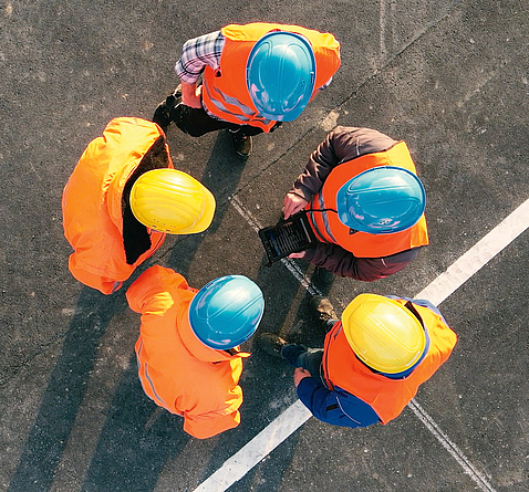 Blick von oben auf einer Gruppe mit fünf Personen, die Schutzhelme und Schutzkleidung tragen.