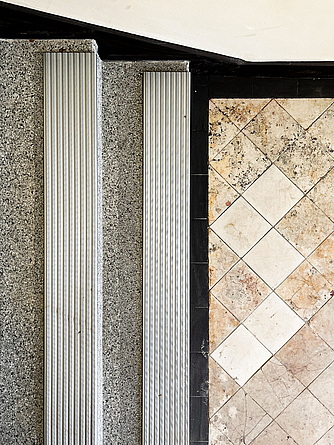 Bauzeitliche Bodenfliesen wurden erhalten. Der Terrazzoboden des Treppenhauses wurde aufgearbeitet oder erneuert und um Stufenprofile ergänzt. Detailaufnahme eines Stücks des Terrazobodens und zwei Treppenstufen mit Stufenprofilen.