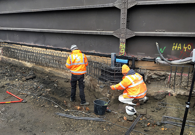 Zwei Personen mit Schutzjacke arbeiten an der Bewehrung des Fundaments.