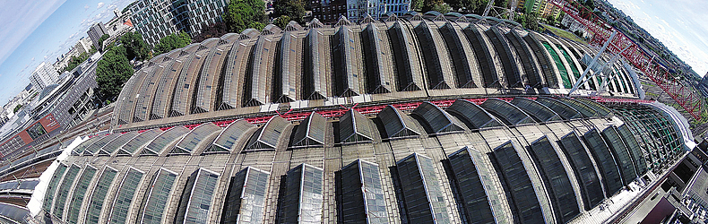 Blick von oben auf die Gleishallendächer mit dem bereits teilweise geöffneten Dach und der Schutzbrücke (August 2022) Drohnenaufnahme, welche die beiden Dächer von oben zeigt.