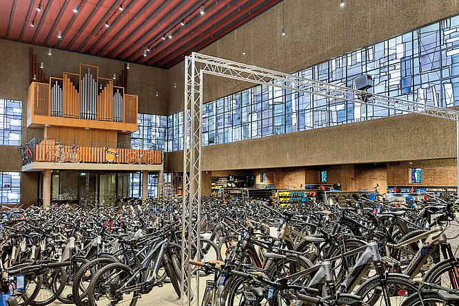 Große Halle mit zahlreichen abgestellten Fahrrädern und einer Orgel auf einer Empore.