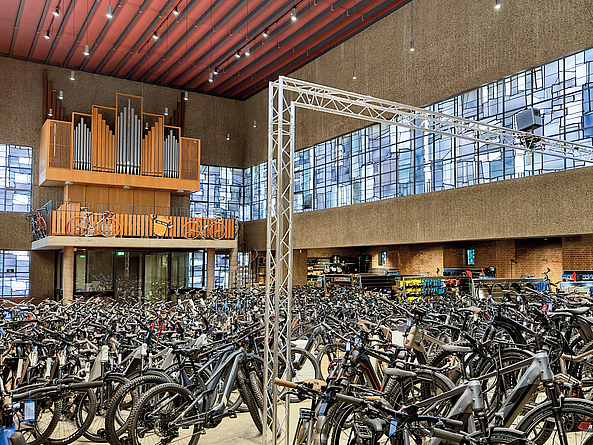 Große Halle mit zahlreichen abgestellten Fahrrädern und einer Orgel auf einer Empore.