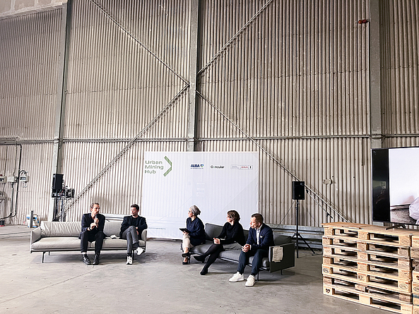 In einer Halle, die als Konferenzraum dient, sitzen fünf Personen zu einer Diskussionsrunde zusammen.