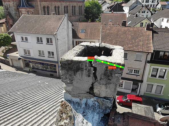 Drohnenbild zeigt Schornstein von oben: Angezeigt werden sein Mauerwerk mit quadratischer Grundfläche, ein 4 Zentimeter breiter Riss und dessen Abstand vom rechten Rand des Schornsteins.