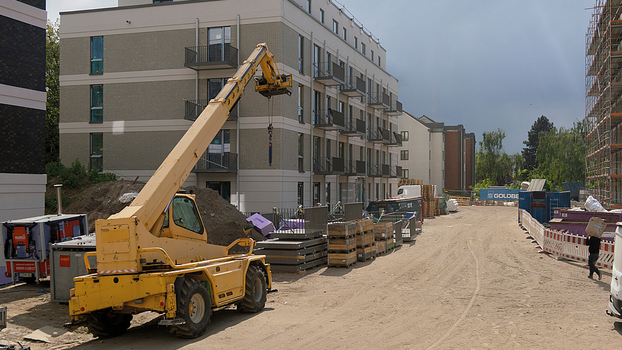 Serielles Bauen Greenpark mit Mobilkran Baustelle mit mehrgeschossigem Neubau, davor befinden sich Fertigelemente und Balkone zum weiteren Anbau sowie ein Kranfahrzeug.