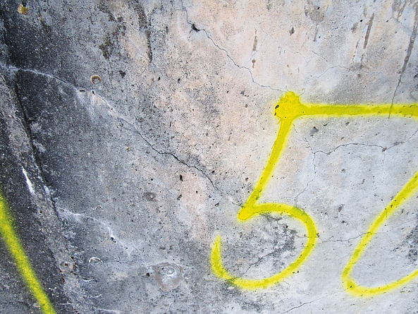 Mit gelben Zahlen markierte Betonflächen mit Rissen und weißen Flecken.